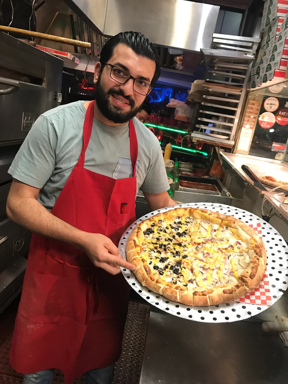 Waleed, owner of Yummy Pizza, holding a fresh pizza in the shop